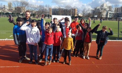 Groupe de jeunes joueurs et leur entraîneur, bras levés, sur la piste du stade avant les championnats d'Île-de-France.