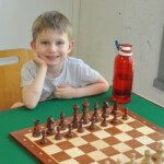 Un jeune joueur souriant, accoudé devant son échiquier prêt pour la partie, en fin de saison au club.
