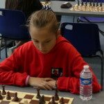 Une jeune joueuse en sweat rouge, concentrée devant son échiquier aux championnats jeunes de l'Essonne.