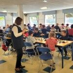 Salle du 22e Open de Gif remplie de joueurs attablés devant leurs échiquiers, une arbitre au premier plan.