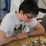 Jeune joueur à lunettes en pleine réflexion devant son échiquier, compétition Loiret-Essonne.