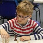 Un jeune joueur en pull rayé déplace une pièce lors des Championnats jeunes de l'Essonne.