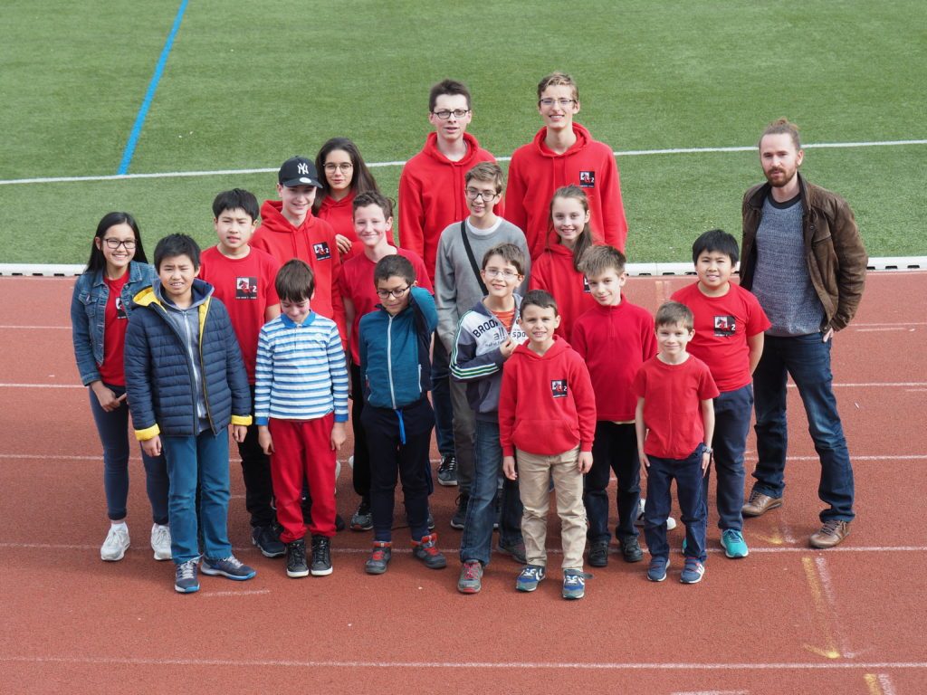 Groupe de jeunes du club en tenue rouge posant sur la piste du stade aux championnats d'Île-de-France.