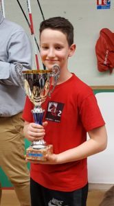 Un jeune joueur en maillot rouge du club brandit fièrement sa coupe après la première étape.