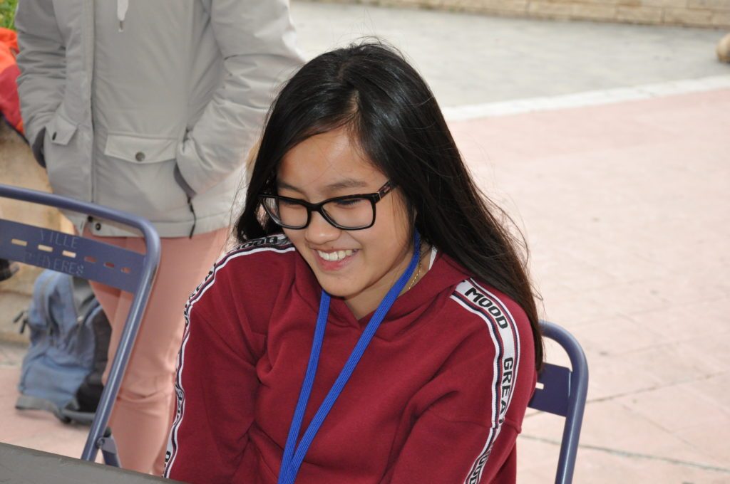 Une jeune joueuse souriante devant son échiquier lors des Championnats de France à Hyères.