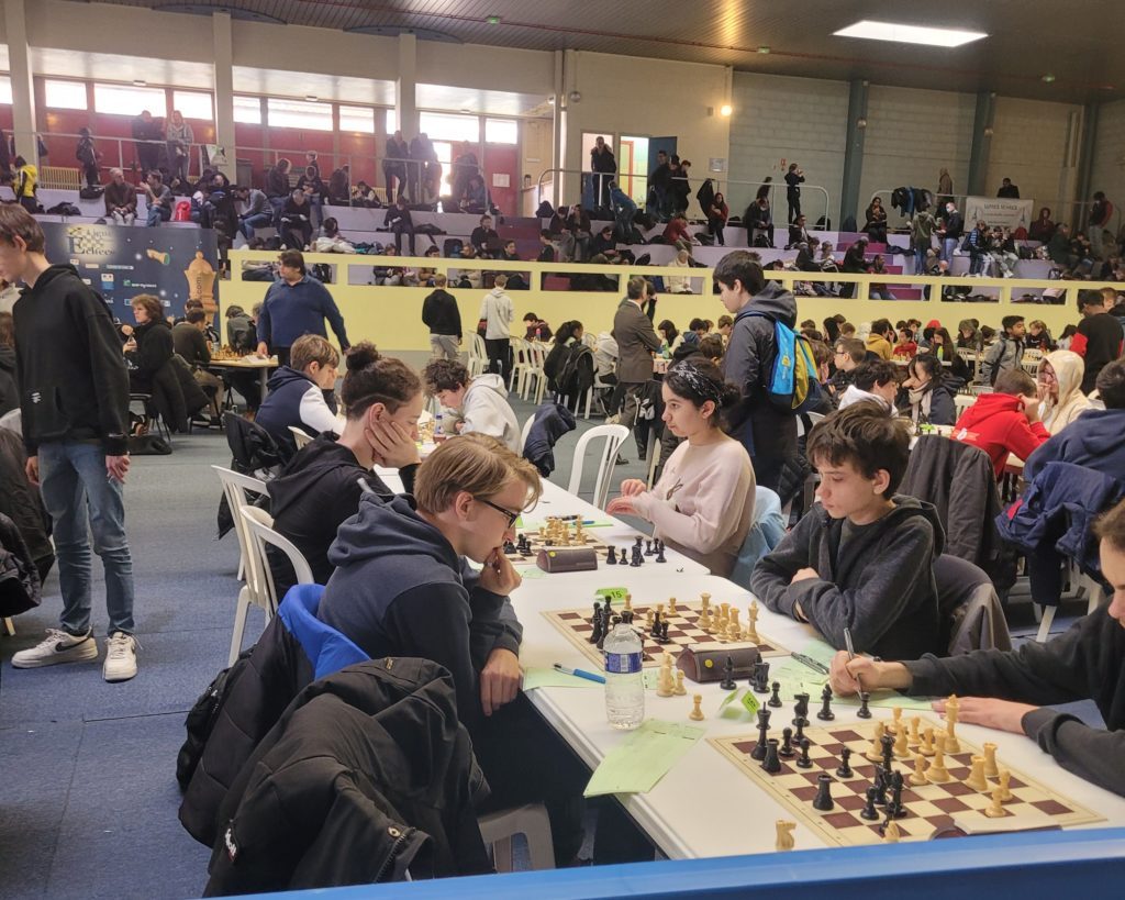 Gymnase rempli de joueurs attablés et de spectateurs en tribune lors des championnats jeunes d'Île-de-France.