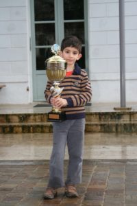 Un jeune joueur tenant fièrement sa grande coupe de champion petit-poussin d'Île-de-France.