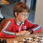 Un jeune joueur à lunettes, en survêtement rouge, concentré sur sa partie lors de la compétition.